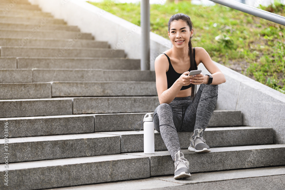 Pretty young asian woman resting after jogging outdoor, sitting on urban stairs