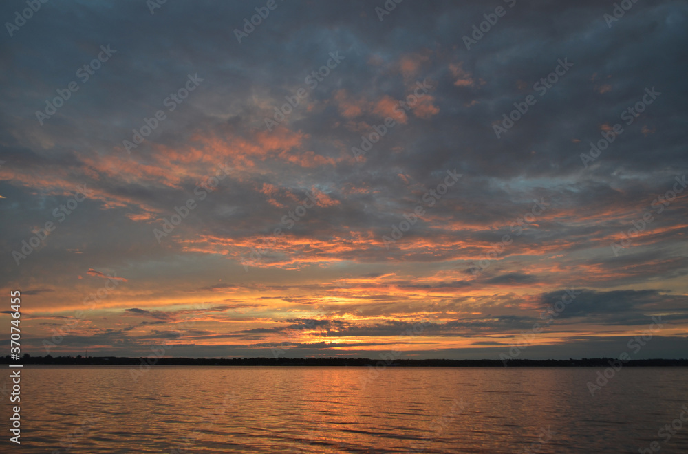 Canadian sunset over a beautiful lake showing a horizon full of colours in pink, gold, orange and teal clouds.