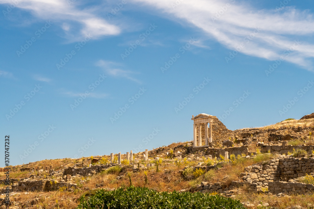 Well preserved Temple of Isis on Delos Island located on the hill above the ancient city with other ruins and blue sky in the background, Greece. Distant view from below, low horizon.