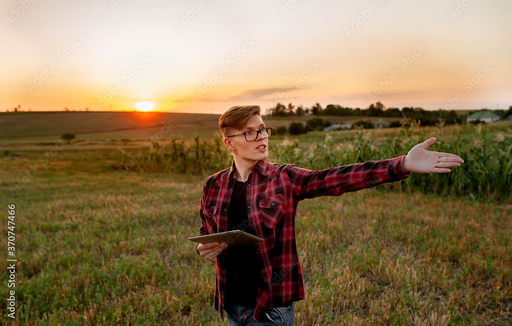 
Farmer with tablet at sunset in the field shows with his hand to the side, agriculture management concept
