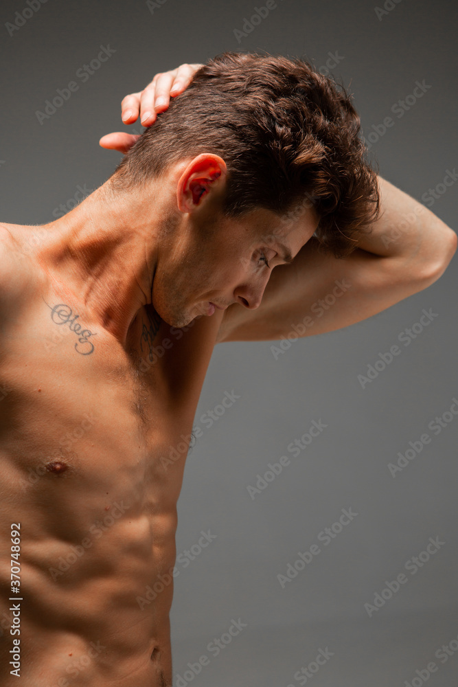 Portrait of handsome young guy with stylish haircut without shirt standing in studio. Body with tattoo