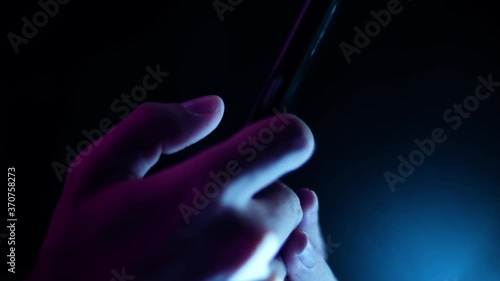 Thumb scrolling and tapping a smartphone close up side profile in a dark room with purple and blue lighting
