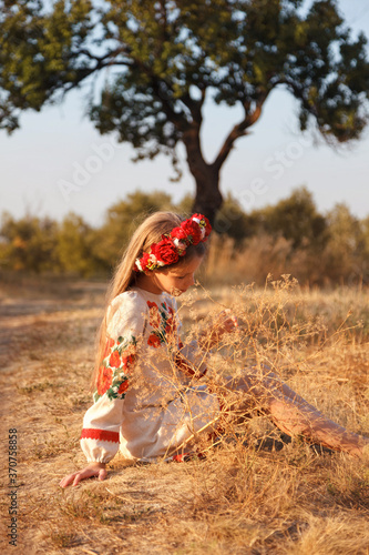 Portrait of a girl in an embroidered shirt in a field at sunset.