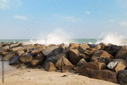 Rocky coastline with long waves lapping with sand and blue sky.