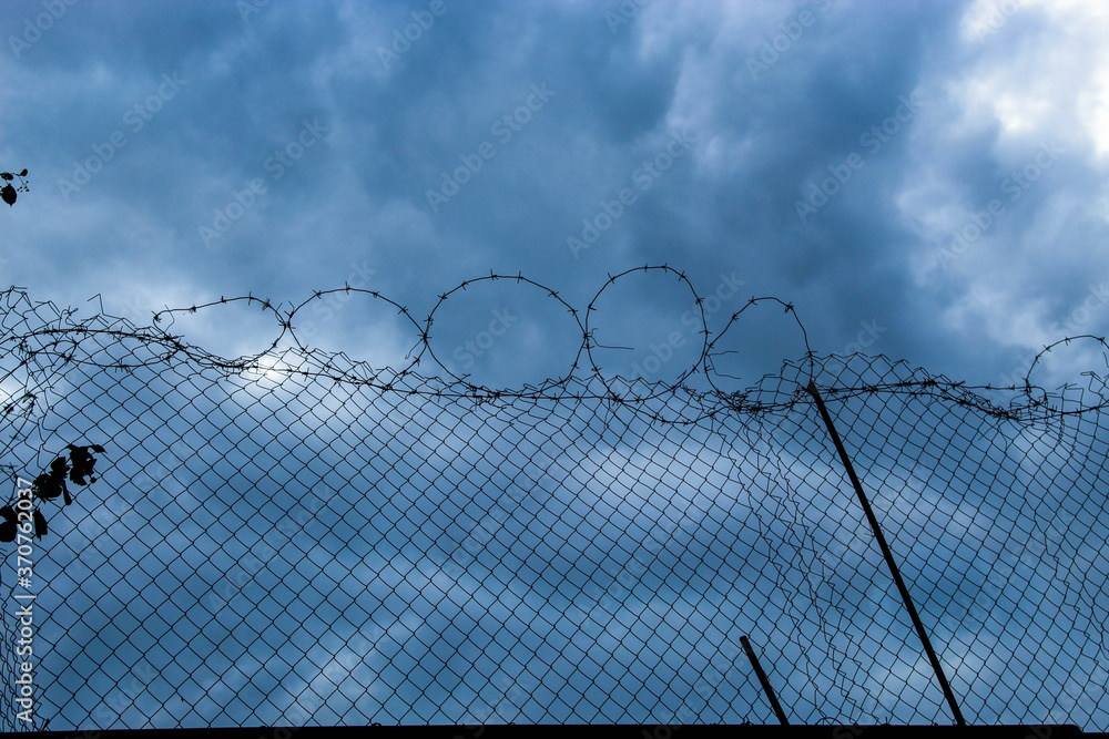 A stone fence with barbed wire at the top against a beautiful blue sky A stone fence with barbed wire at the top against a beautiful blue sky