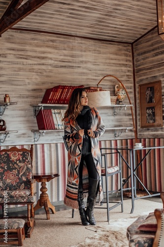 Beautiful model posing for photos in a room. Wearing black pants, boot and colorful blouse.