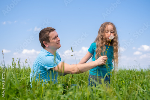 father and daughters spending time. Dad and daughters playing together on field green grass at summer. girl blowing on a dandelion