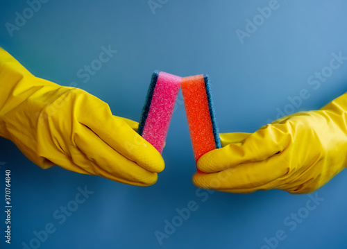 yellow gloves hold dishwashing sponge on blue background