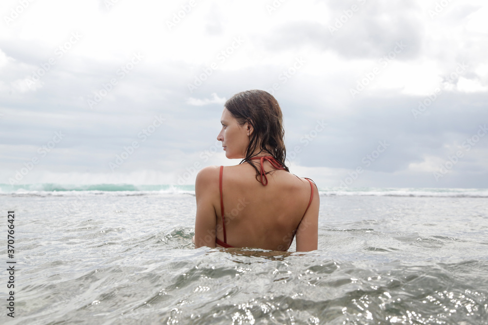 Back view of a young woman in the ocean enjoying cool ocean water during vacation. Freedom and happiness concept. Back view of a young woman in the ocean enjoying cool ocean water during vacation. Freedom and happiness concept.