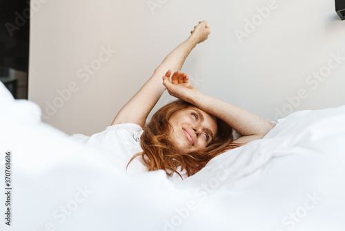 Image of woman stretching her body while lying in bed after sleep
