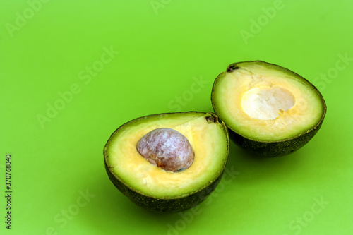 Fresh ripe avocado cut in half on the green background. Antioxidant snack and healthy eating concept. Space for text