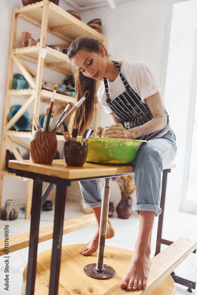 Young female ceramist working by using pottery wheel indoors and making handmade clay product Young female ceramist working by using pottery wheel indoors and making handmade clay product