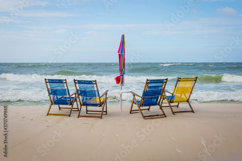 Four empty beach chairs facing the ocean with an umbrella