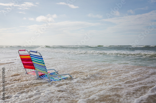 Two empty beach chairs facing the ocean and being overtaken by incoming tide