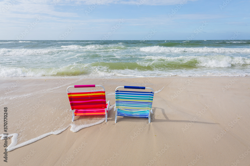 Two empty beach chairs facing the ocean and being overtaken by incoming tide Two empty beach chairs facing the ocean and being overtaken by incoming tide