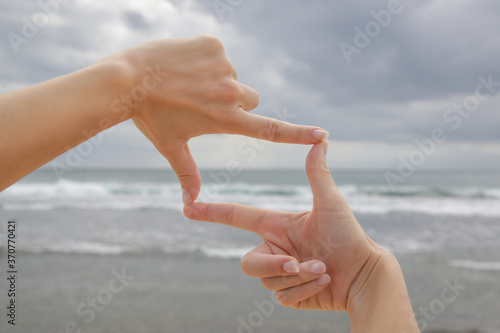 Woman holds hands in the shape of a frame in front of blue ocean horizon © triocean