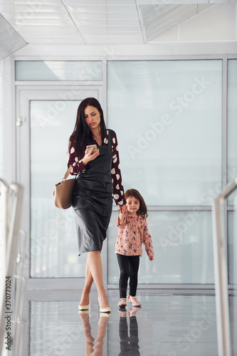 Young mother with her daughter walking together indoors in the office or airport. Having vacation © standret