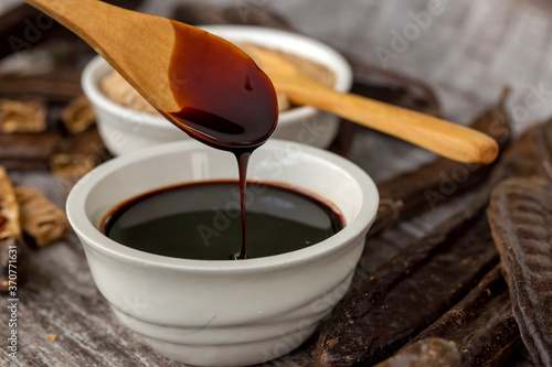 Carob molasses and carob pods on wooden background photo