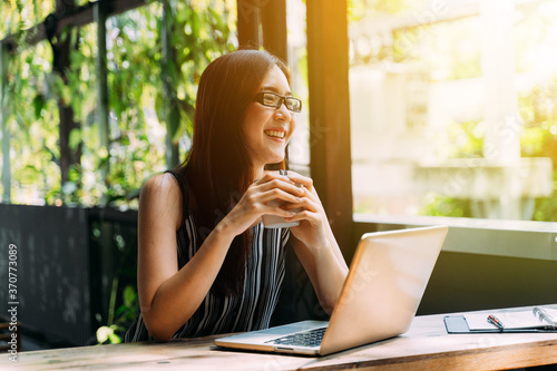 Canvas-taulu Positive Asian female student in glasses smiling and browsing laptop while sitti