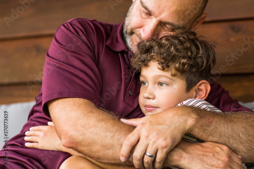 Fotografija Hispanic father sitting and hugging his son.