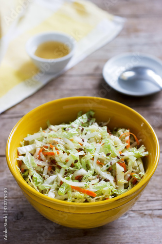 Coleslaw of cabbage, carrots and various herbs with mayonnaise in a large plate on a wooden background.