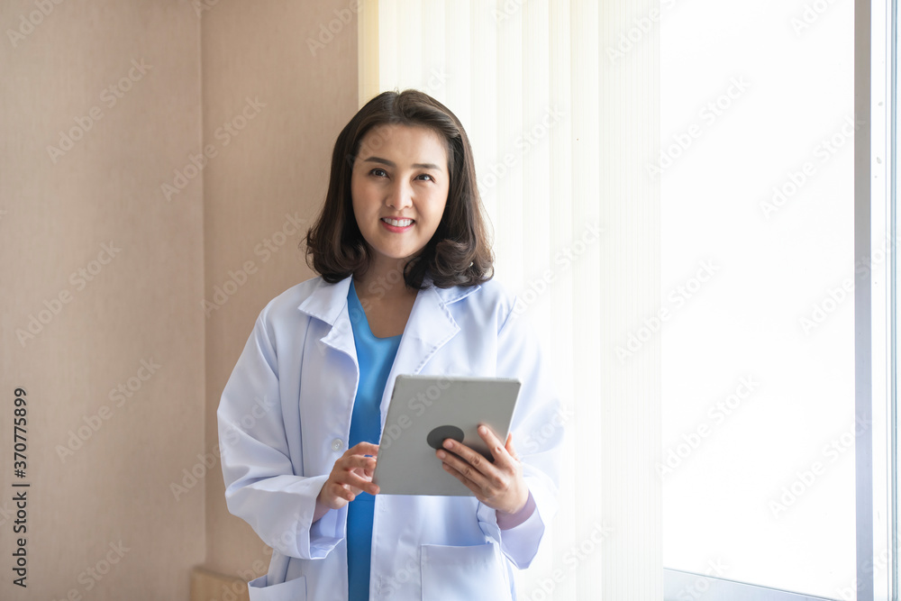 Female doctor orthopedist use tablet in office hospital. Confident female doctor sitting at office desk and smiling at camera, health care and prevention technology concept Female doctor orthopedist use tablet in office hospital. Confident female doctor sitting at office desk and smiling at camera, health care and prevention technology concept