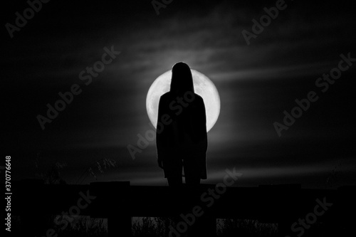 Silhouette of a woman standing in the darkness with full moon