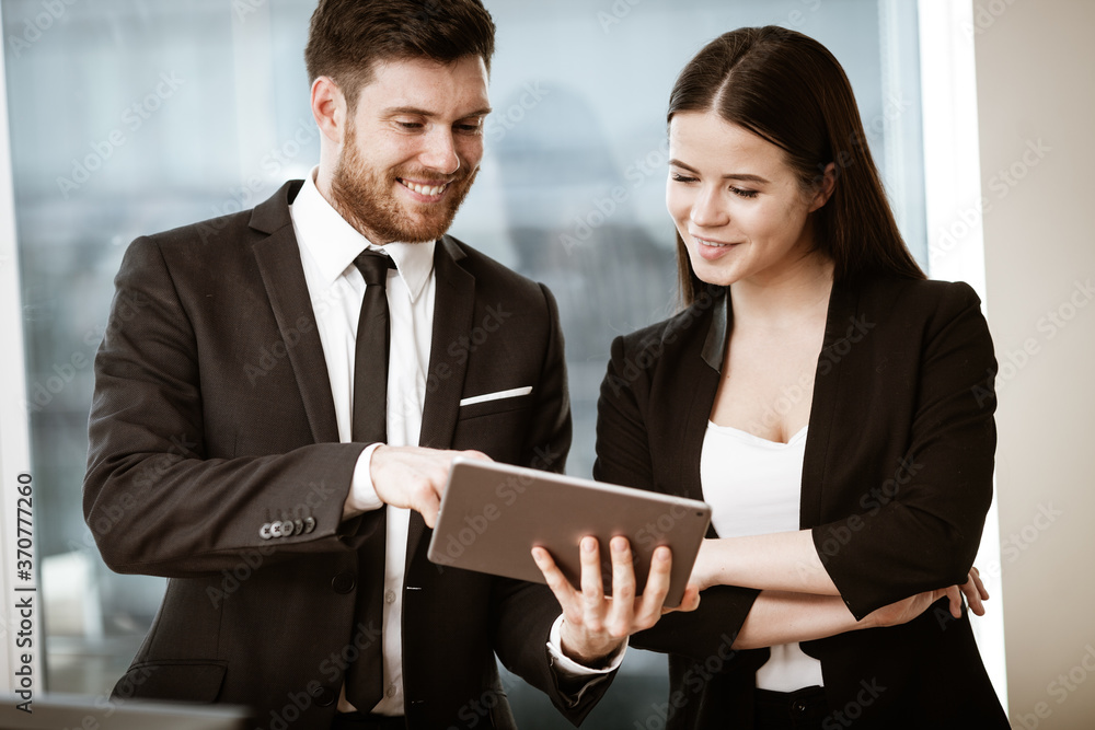 Successful business and modern technology concept. Young businesswoman and happy smiling businessman working together using tablet computer. Two colleagues man and woman teamwork indoors. Successful business and modern technology concept. Young businesswoman and happy smiling businessman working together using tablet computer. Two colleagues man and woman teamwork indoors.