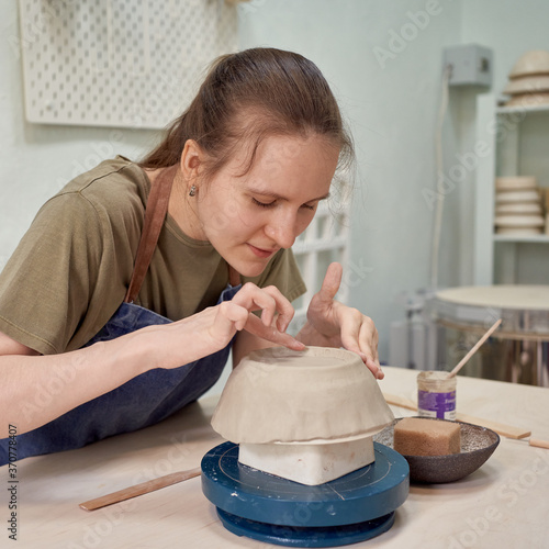 Concentrated young woman ceramist working on clay ware with satisfaction as recreation in creative art studio photo