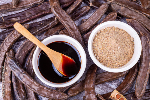 Slika na platnu Carob molasses and carob pods on wooden background