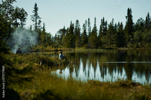 A young girl fishes at a beatiful lake in the deep and wild forest of Norway. Alone in the relaxing nature.