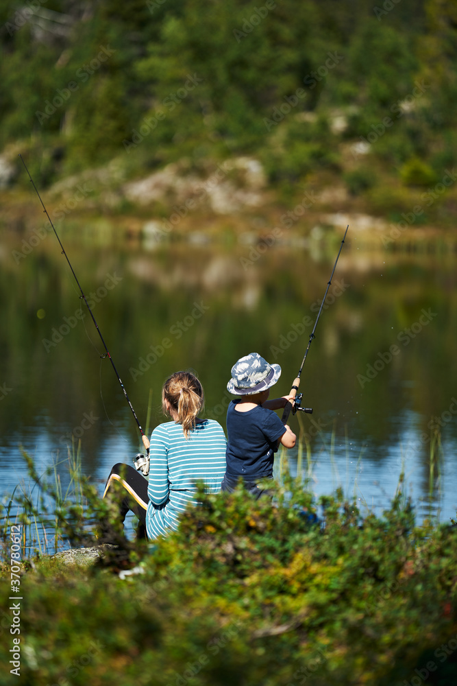 A young girl with her little brother fishes in a small lake.  Shot in the deep wild forest of Hallingdal, Gol, Norway.