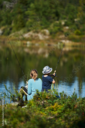 A young girl with her little brother fishes in a small lake. Shot in the deep wild forest of Hallingdal, Gol, Norway.