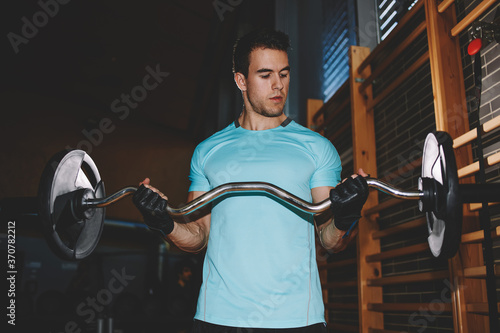 Athletic man pumping up muscules with dumbbell, attractive young man training indoor, man doing heavy dumbbell exercise for biceps, muscular bodybuilder man doing exercises with dumbbell in gym photo