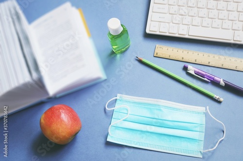 School reopening during coronavirus COVID-19 pandemic. Table in classroom fla tlay photo. Open book, face mask, sanitizer gel, computer, stationery photo