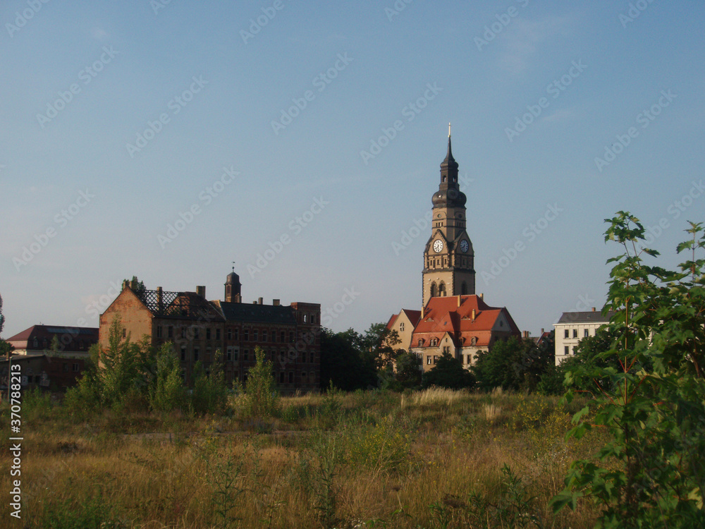 View of church and other buildings across overgrown field in the Plagwitz neighborhood of Leipzig, Germany.