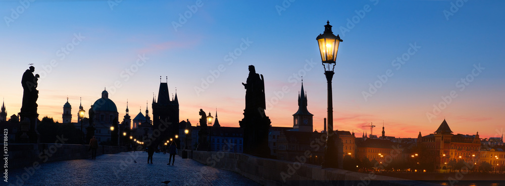Charles Bridge at dawn. Panoramic image, silhouette of Bridge Tower and sculptures, street lights in Prague, Czech Republic.