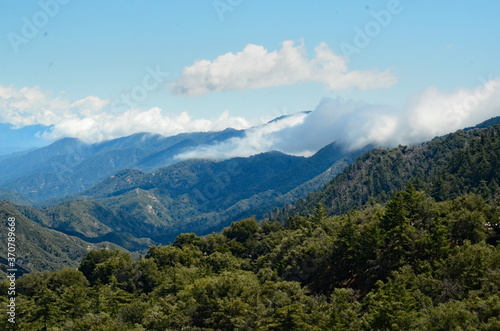 Beauful mountain landscape, white puffy clouds hover over part of mouintain range, looks like mountain has a blanket of clouds on, green slopes, blue sky and inspiring.