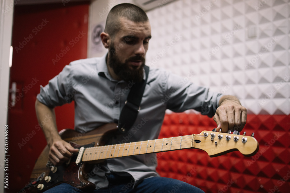 Obraz premium Guitar player setting his music instrument in studio. Rock band member doing rehearsal and setting his guitar before recording audio.