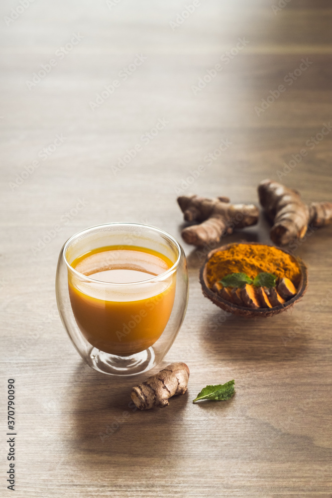 Organic orange turmeric drink, tea with cinnamon in a glass mug with fresh turmeric powder on wooden background. Indian oriental low cholesterol spices. Food and drink, diet nutrition Organic orange turmeric drink, tea with cinnamon in a glass mug with fresh turmeric powder on wooden background. Indian oriental low cholesterol spices. Food and drink, diet nutrition