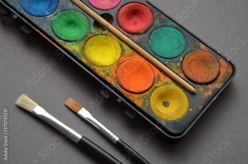Colorful watercolor paint and brushes with a grey background