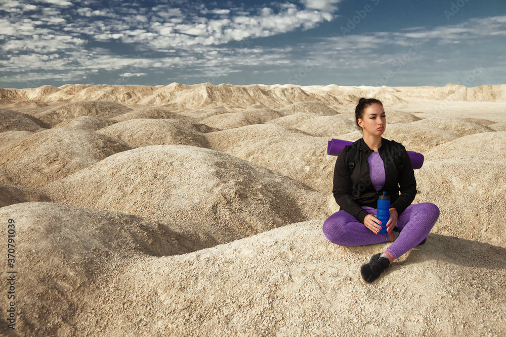 woman with backpack sitting on yellow dunes looks into distance on sunny day, copy space