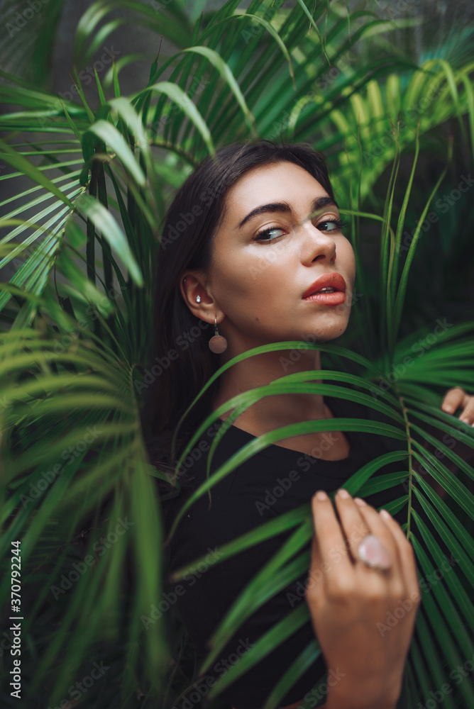 beautiful brunette with mother of pearl earring peeks out of green bushes. beautiful brunette with mother of pearl earring peeks out of green bushes.