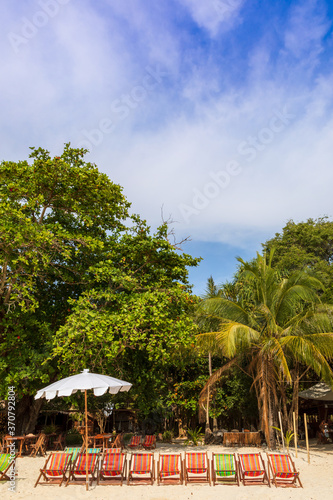 An umbrella and several sun loungers on a beautiful tropical beach and a sea view with a coconut tree
