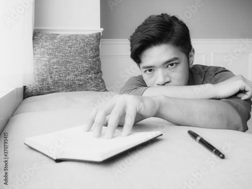 Young asian man taking break after reading book at home in black and white