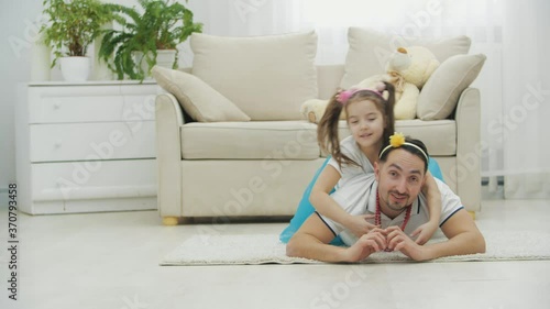 Cute little child with nice pigtails is lying on father's back. He dumps her to the floor and they both show thumbs up, smiling. photo