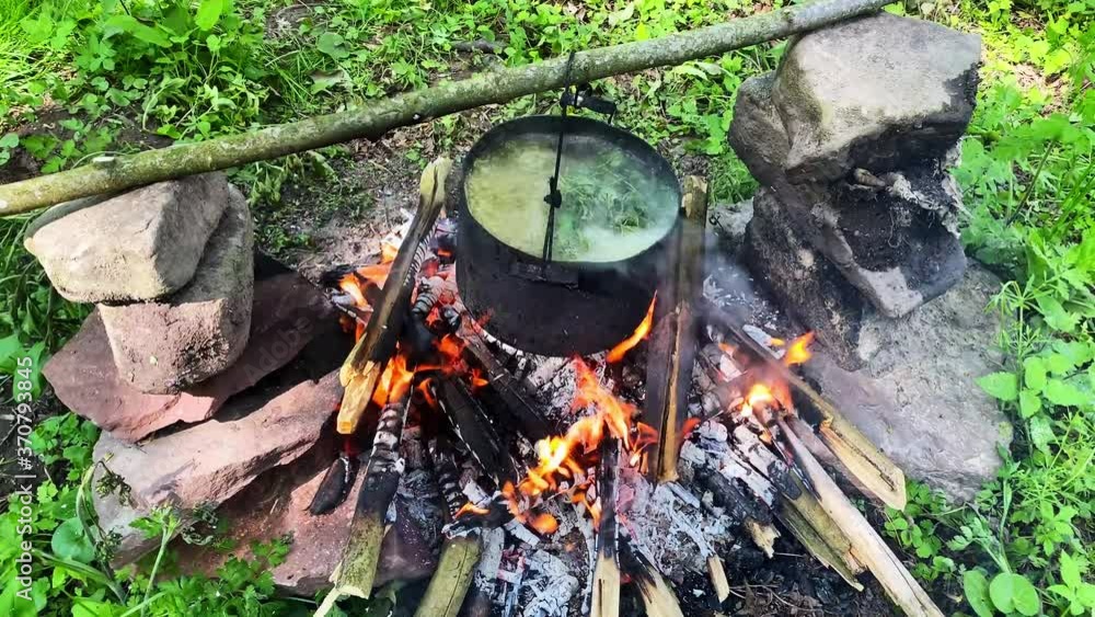 Cooking outdoor food in tourist pot at bonfire. Process preparing camping food on burning fire while hiking to wild nature Cooking outdoor food in tourist pot at bonfire. Process preparing camping food on burning fire while hiking to wild nature