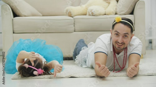 Lively father is playing with his daughter, lying on the floor, teaching her to give thumbs up. photo