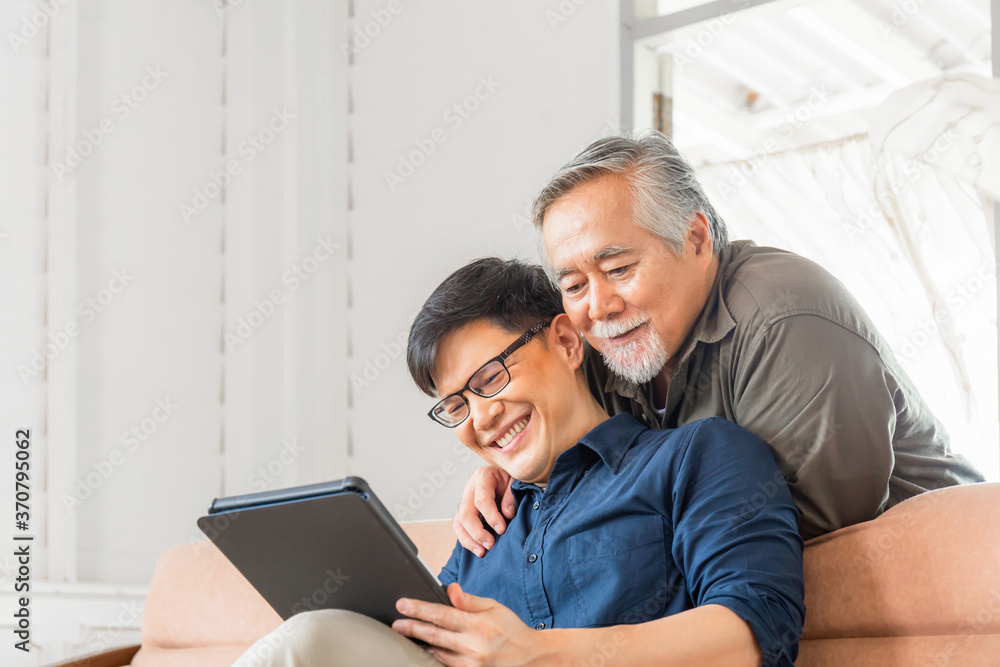 Happy senior asian father and adult son using tablet smartphone in living room Happy senior asian father and adult son using tablet smartphone in living room