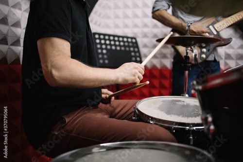 Male hands with drumsticks playing on drum set. Cropped drummer playing cymbals and drums and sitting in soundproof room.